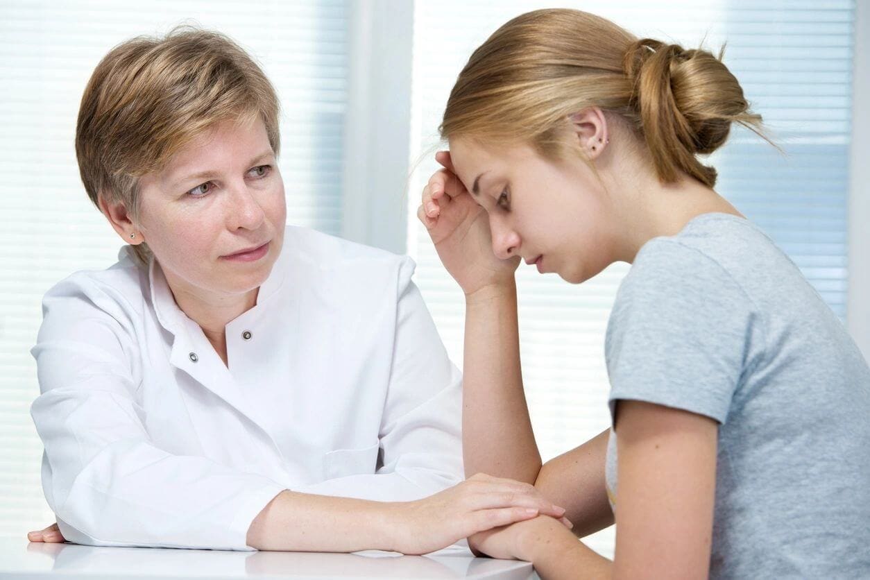 A woman sitting next to a doctor with her hand on the forehead of another person.