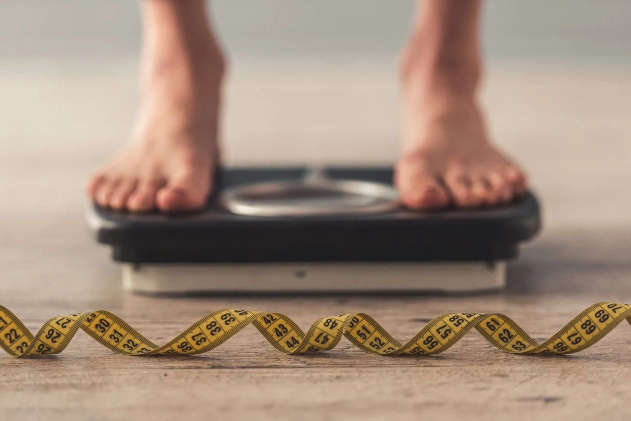 A person standing on a scale with a tape measure in the foreground.