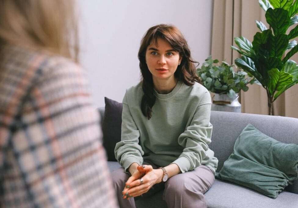 A woman sitting on the couch talking to another person.